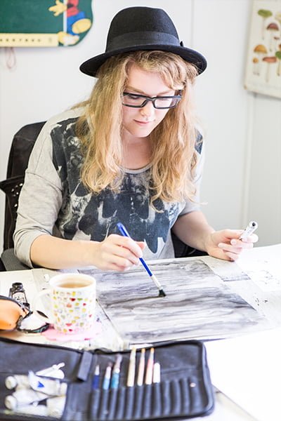 Sarjakuvalinjan opiskelija maalaa pöydän äärellä
