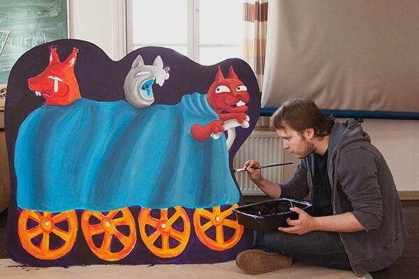Sarjakuvalinjan opiskelija maalaa maalausta, jossa on kolme hahmoa